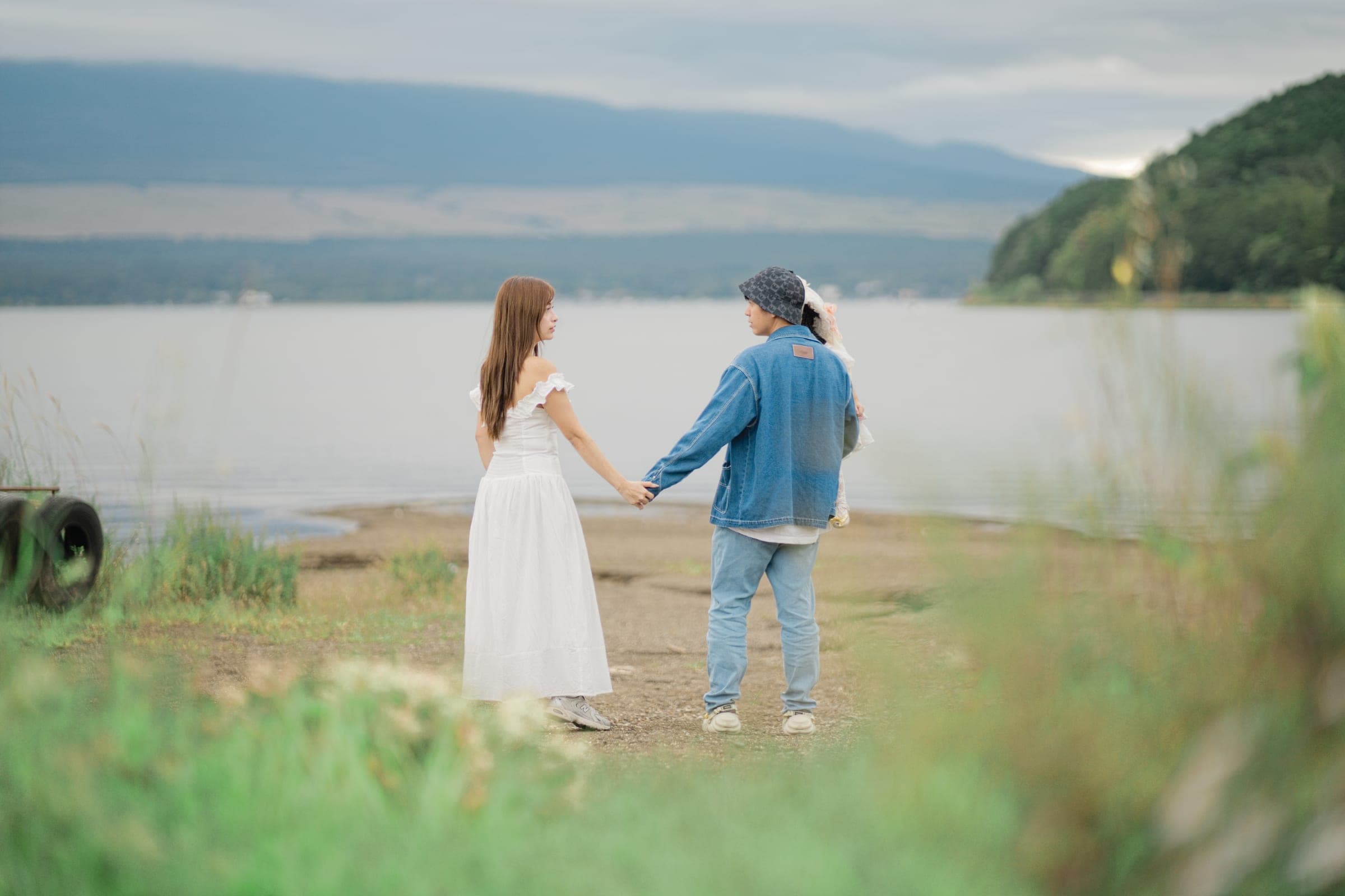 A couple holding hands at the edge of a lake, mountains across the water