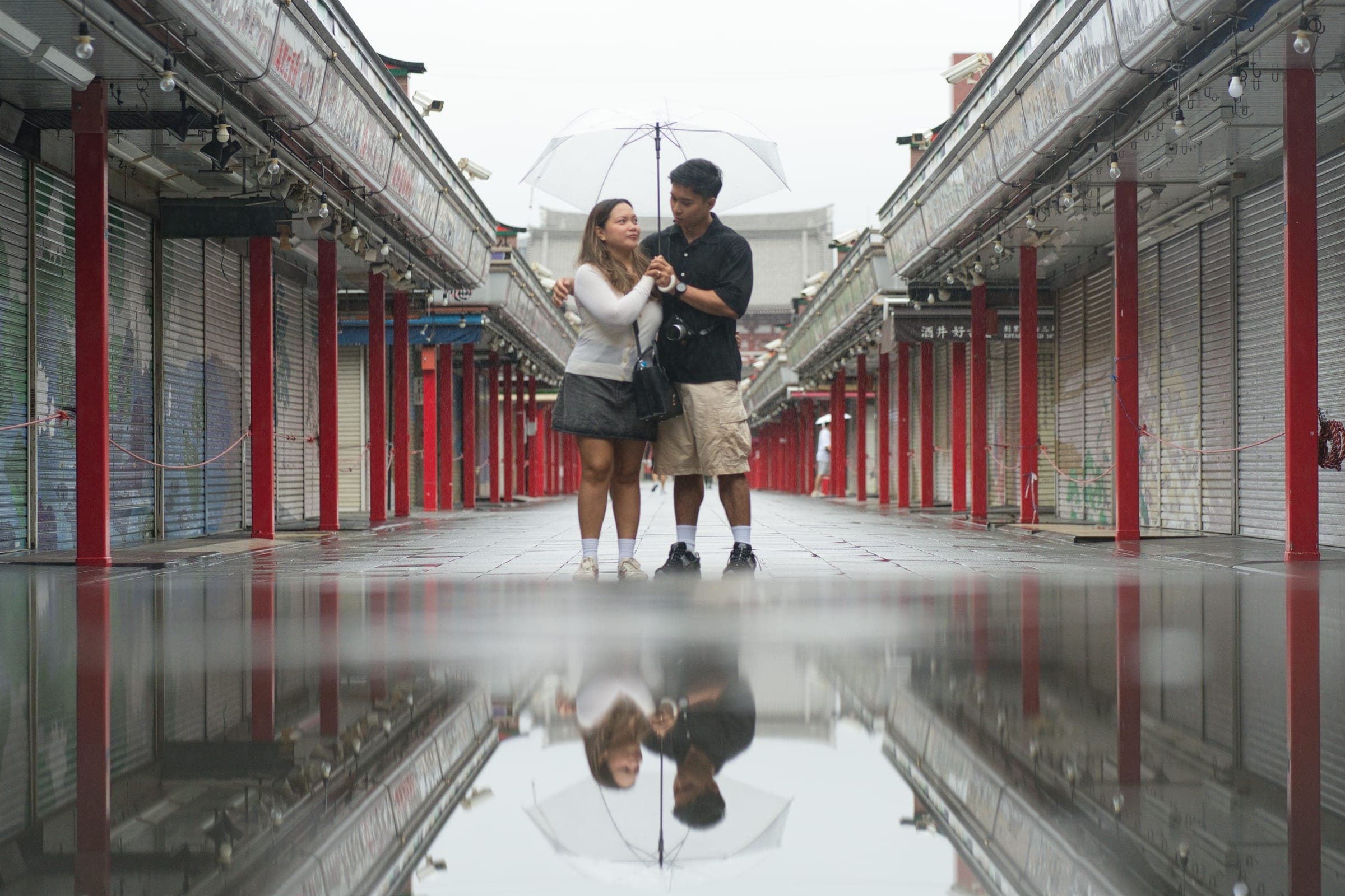 A couple reflected in wet pavement on the approach to Sensō-ji