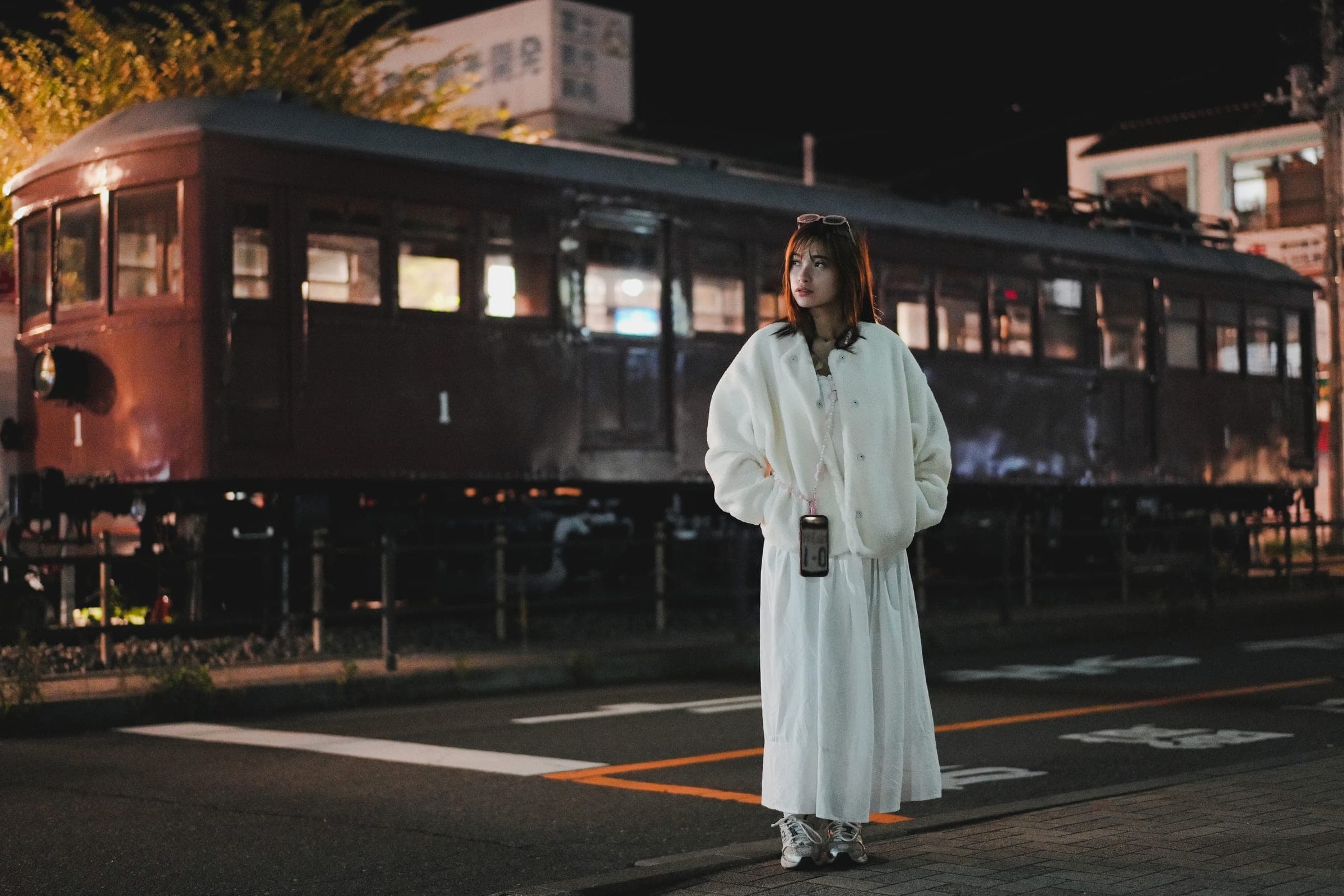 A woman in white beside a vintage red train carriage after dark